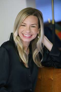 Dr. Jessica Jeffrey wearing a black shirt, smiling at the camera with her arm resting on the desk