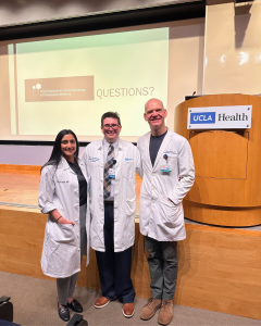 Three medical professionals in lab coats pose on stage at a UCLA Health event.