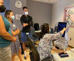 Clinician points at ultrasound monitor while three masked observers watch