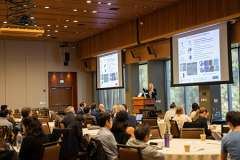 Presentation at a conference with an audience and slides on screens.