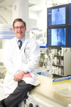 Doctor with glasses sitting on a desk smiling