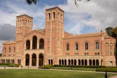 Royce Hall, a historic red brick building with towers, surrounded by green landscaping.