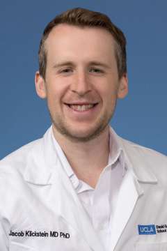 Smiling person in white lab coat and collared shirt on blue background