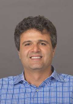 Dr. Peyyman Golshani, a man with dark, wavy hair, smiles warmly while wearing a blue plaid button-up shirt.