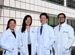 Four individuals in white lab coats standing outside a modern building.