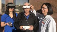 Dr. Chun, right, demonstrates examples of two of the wearable electronic headset devices that use image enhancement to improve vision while performing tasks at far distances, intermediate and/or near