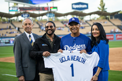 Four people pose at Dodger Stadium, holding a Dodgers jersey with “UCLA Health” and the number 1 on the back.
