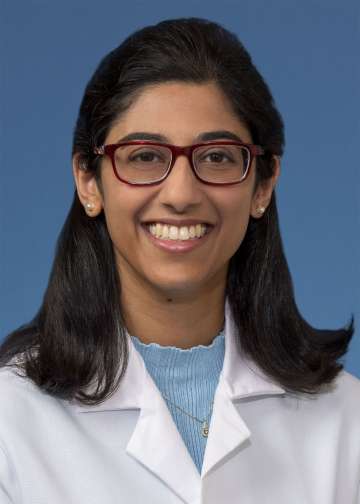 Smiling person in white lab coat and red glasses on blue background.