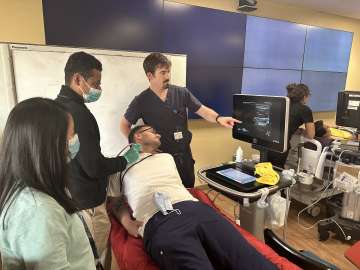 3 students performing an ultrasound on a man's neck