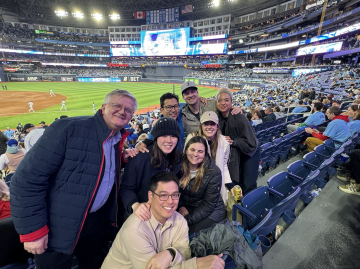 Eight anesthesiologists, four men and four women, posing for the camera while enjoying a baseball game.
