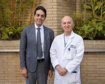 Two men standing outdoors, one in a suit and the other in a doctor's coat.