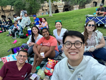 Group of friends enjoying a picnic on grass with snacks and chairs in a park.
