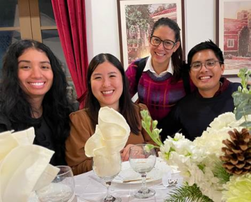 Group of four people at a dining table with floral decor and glasses.