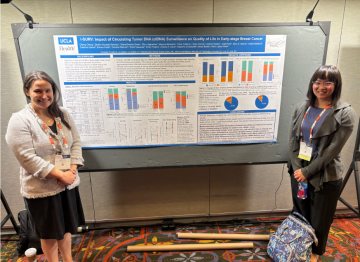 Cheng Cheng, who has dark hair and bangs in front of her research poster with her mentor, who is wearing a white jacket.