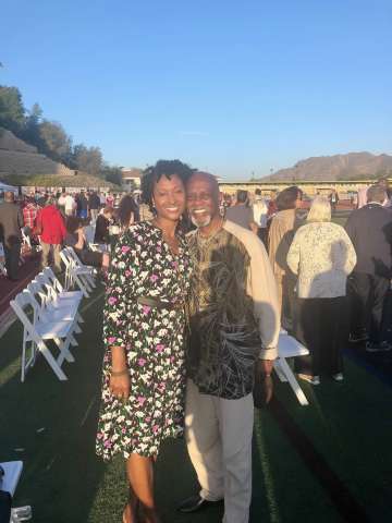 Two people smiling and embracing at a sunny outdoor event