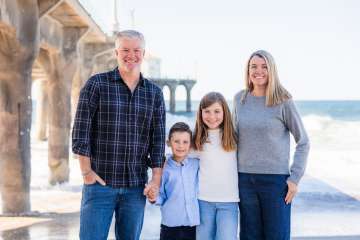 Two adults and two children standing on a beach pier with ocean behind them