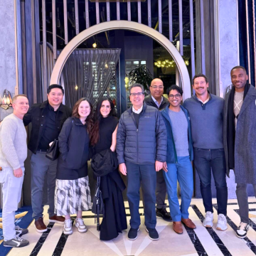 Group of ten adults standing and smiling before a circular gold mirror in a lobby.