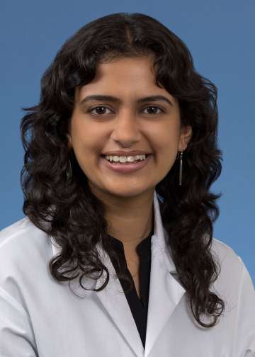 Head shot of Anjali Upadyaya in a white coat, smiling at the camera