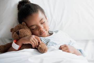 Child patient laying with teddy bear in hospital bed