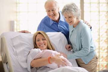 Mother holding newborn in hospital bed while grandparents are standing beside