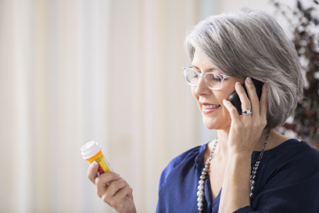an elderly woman on the phone looking at a prescription medication bottle
