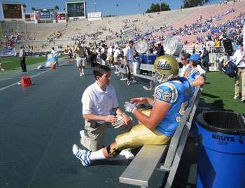 UCLA Football player sitting on the bench talking to a sports medicine doctor.
