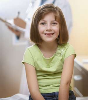 Young girl wearing a green shirt sitting on a hospital bed smiling