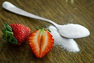 Strawberries next to spoon with sugar