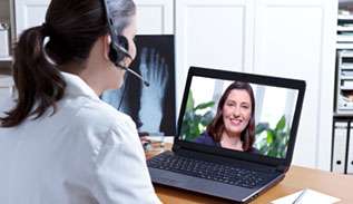 Woman wearing headset and speaking to a patient on her laptop