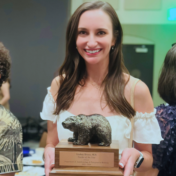 Lindsay Brown, MD holding her DAPM Teacher of the Year award. Wooden base with a copper bear on top.