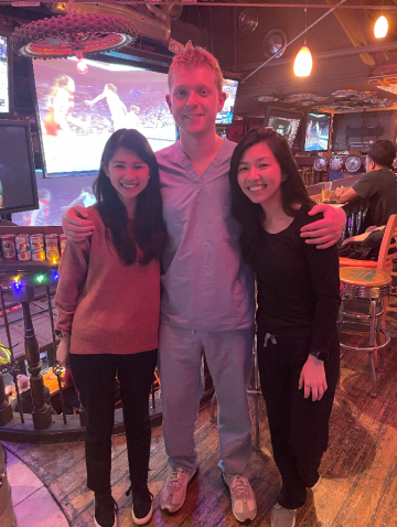 Three neurology chief residents, one man standing center with his arms around two women, one on either side, smiling at the camera