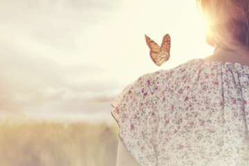 Woman standing in a field outside with a butterfly on her shoulder