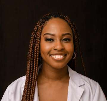 Head shot of Angela Udongwo in a white coat, smiling at the camera