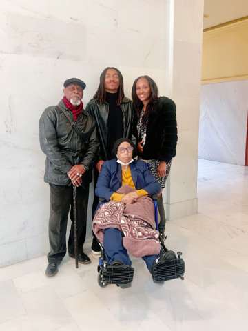 Group portrait: three standing adults with a person in a wheelchair