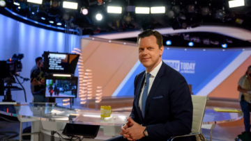 Willie Geist in a suit at TV studio desk with cameras and monitors behind