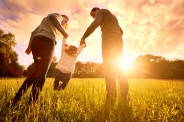 Parents lifting their kid on a grass field during sunset