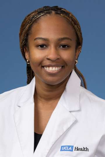 Head shot of Angela Udongwo, MD, MPH, in white coat, smiling at camera