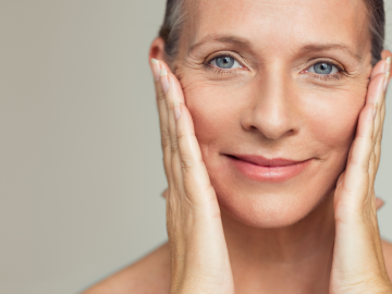 Close-up of a middle-aged woman gently holding her cheeks, highlighting smooth skin and content facial expression.