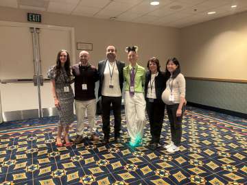 Six conference attendees wearing badges posing together in a hotel meeting room