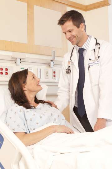 Doctor standing by female patient's bedside smiling