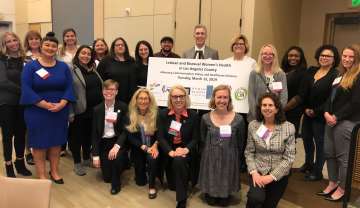 Group photo of diverse individuals posing together, holding a large sign.