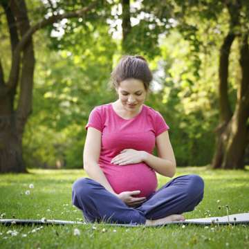 Pregnant woman sitting on grass holding her belly
