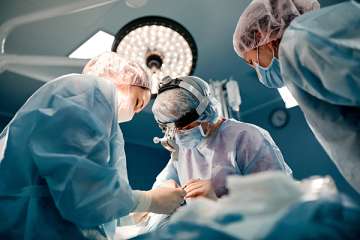 Four surgeons in a brightly lit operating room perform surgery on a patient.