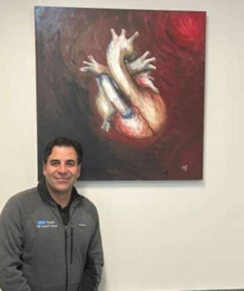 Smiling man next to large stylized anatomical heart painting.