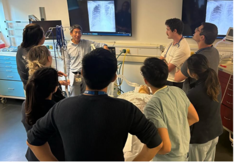 a group of Internal Medicine Residents around a simulated clinic bed for training