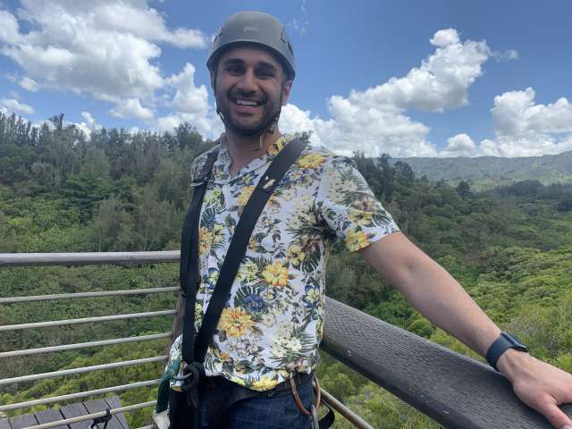 Smiling man in helmet and safety harness on viewing platform over forest.