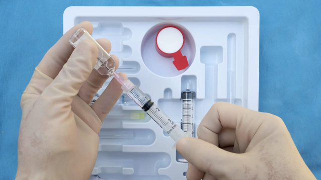 A person holding a syringe and extracting liquid from a small Anesthesia vial