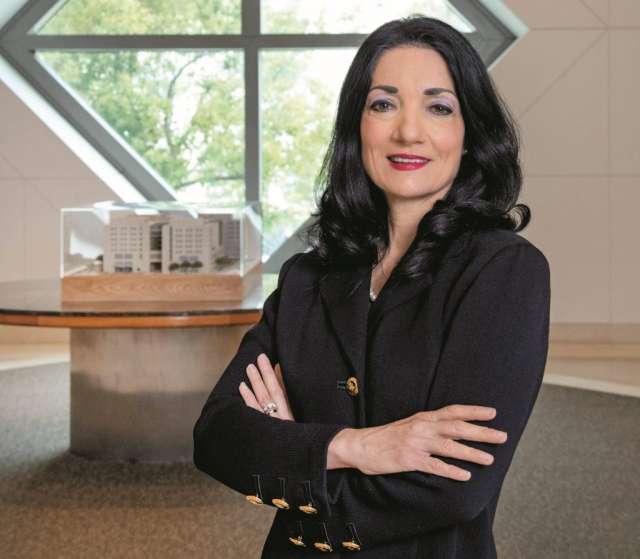 Johnese Spisso stands with her arms crossed, wearing a black blazer. Her relaxed pose suggests she is approachable and confident.
