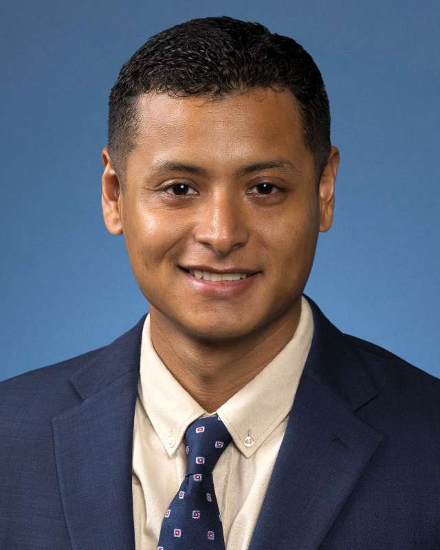 Ezequiel Andrade, MD, in a suit and tie, smiles warmly for the camera, exuding confidence.