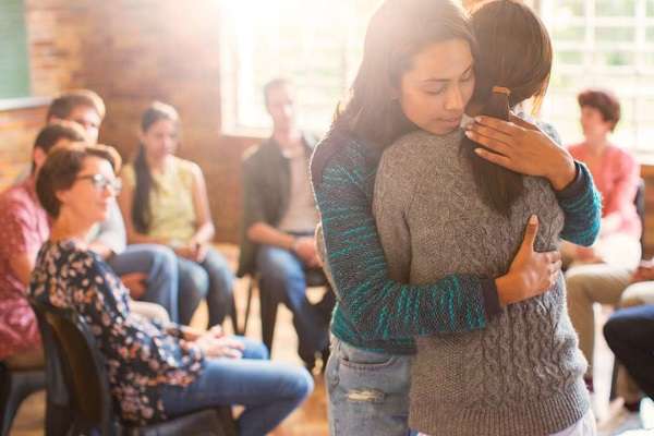 Two people hug each other in a support group setting.